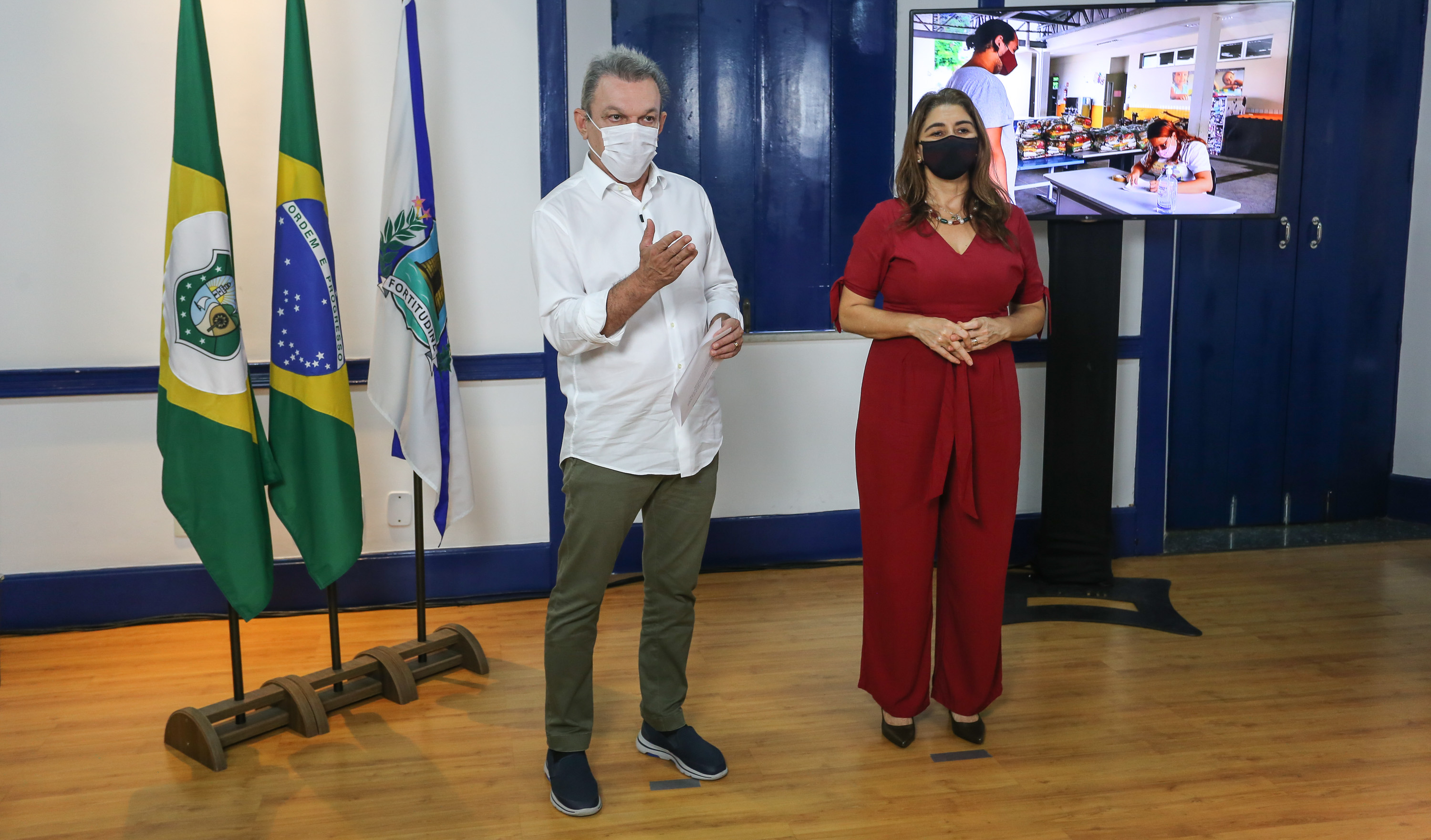 prefeito sarto e secretária dalila em pé, em frente a uma tela de TV